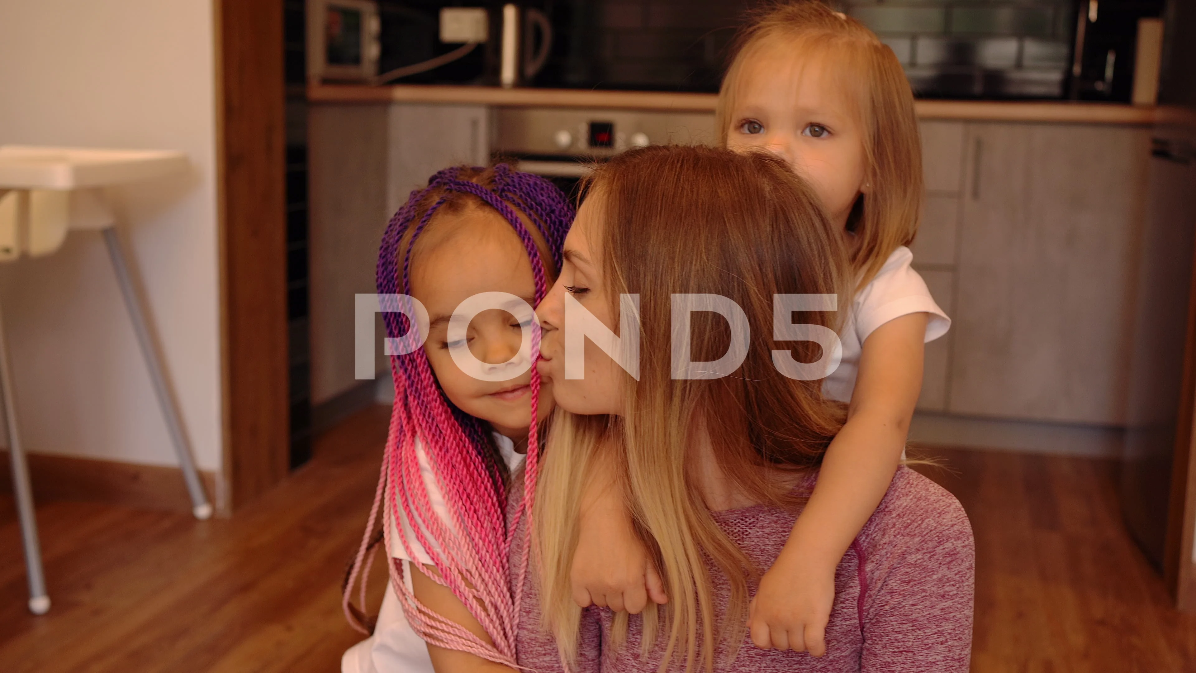 Children kiss mother. Mom and two daughters sitting on the floor hugging