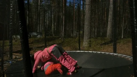 Children, little girls, jump on trampoline in park at spring day Stock Footage