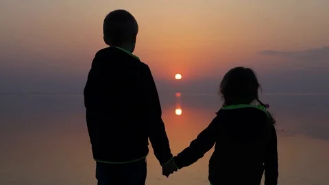 Children looking at sunset under calm water Stock Footage 127437497