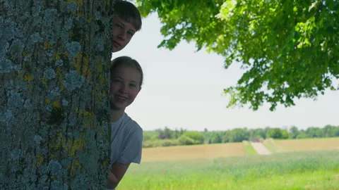 Children Peeking From Behind Tree Trunk in Scenic Nature Stock Footage 339032758