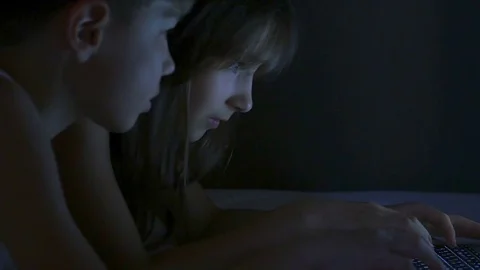 Children play on the computer in the bed under the blanket at night. Stock Footage 77168118
