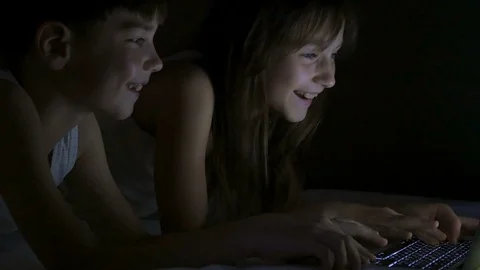 Children play on the computer in the bed under the blanket at night. Stock Footage 77169010