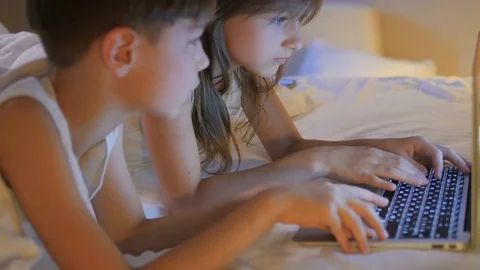Children play on the computer in the bed under the blanket at night. Computer ga Stock Footage 77578814