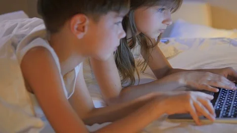 Children play on the computer in the bed under the blanket at night. Computer ga Stock Footage