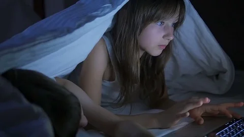 Children play on the computer in the bed under the blanket at night. Stock Footage 80316214
