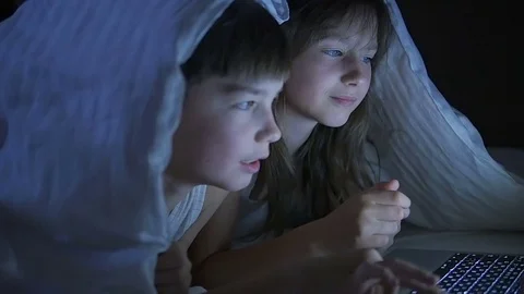 Children play on the computer in the bed under the blanket at night. Stock Footage 80316299