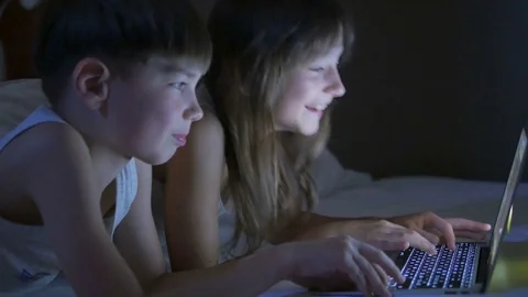 Children play on the computer in the bed under the blanket at night. Stock Footage 80423896