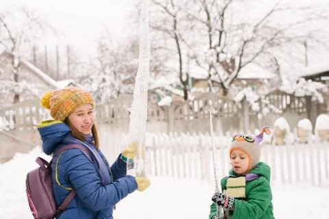 Children play with icicle in snow. Outdoor fun in snowy park by cold weather. Stock Photos