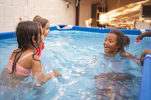 Children play joyfully in a backyard pool during summer afternoon Stock Photos