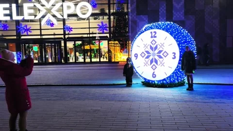 Children play by a large decorative clock in a city square during a holiday even Stock-Footage 325807706