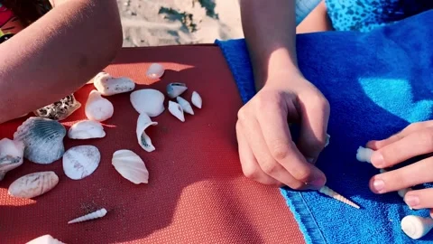 Children play with shells and lay down them on a blue beach towel. Stock Footage 267225207