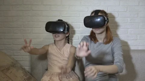 Children play virtual games. Two sisters in virtual reality glasses sit and play 스톡 동영상 98451591
