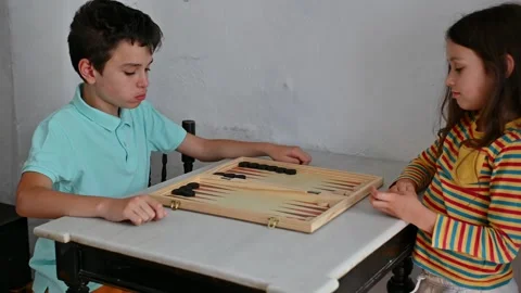 Children playing backgammon at a wooden table indoors Stockbeeldmateriaal 290050307