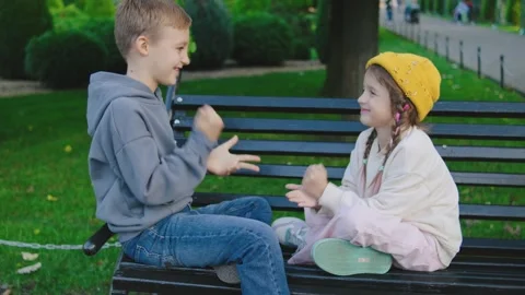 Children playing clapping games on a park bench during a sunny afternoon in a Stock Footage 305418940