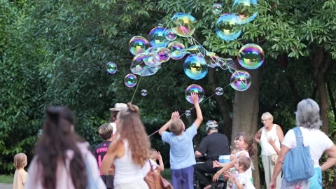 Children playing with large soap bubbles in a park during a performance Stock Footage 340279705