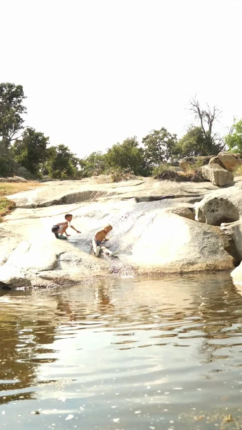 Children playing in a natural pool by jumping from a rock in summer Stock Footage 277454010