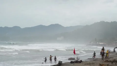 Children playing on a polluted beach with heavy waves and a red warning flag. Stock Footage 331155039