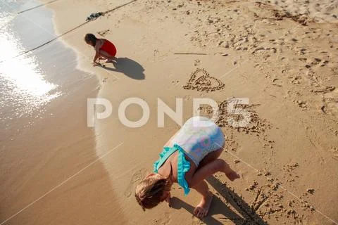 Children playing on the sand beach, little girls drawing heart ,Summer travel Stock Photos
