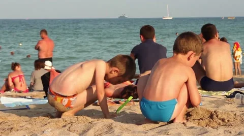 Children playing in the sand on the seashore, while parents looking at the boats Stock Footage 60594984