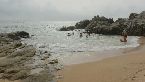 Children playing in the sea waves between rocks in Lloret del Mar, Spain Stock Footage 230096614