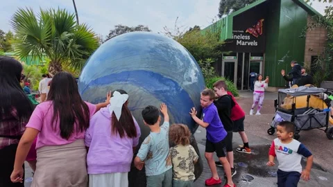 Children pushing a large spinning globe fountain at the San Diego Zoo Safari Stock Footage 338179654