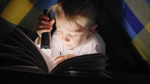 Children read a book under a blanket with a flashlight Stock Footage 166024940