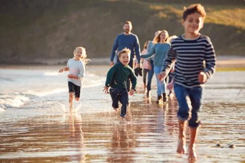 Children Run Ahead As  Multi-Generation Family Walk Along Shore On Winter Beach Stock Photos