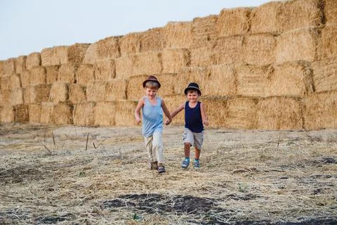 Children run, holding hands, haystack Stock Photos