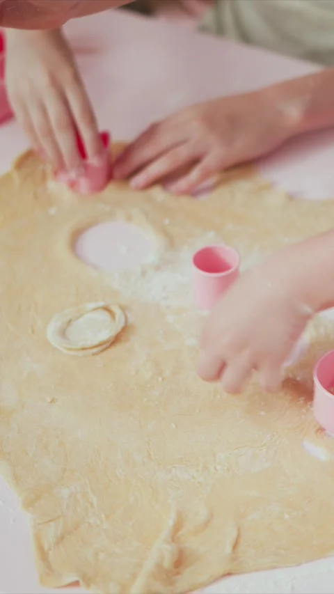 Children shaping soft yellow dough with pink circular cookie cutters in close up Stock Footage 345980186