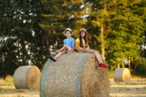Children sit on a haystack with their legs hanging down Stock Photos