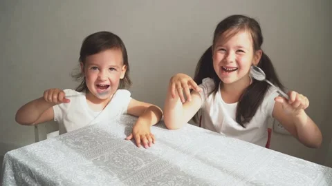Children sit at the table and demand food. Girls bang spoons on the table. The Video stock 157618392