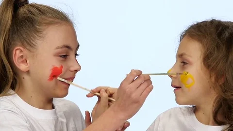 Children sit at the table and paint themselves on their faces with paint brushes Stock Footage 76128421