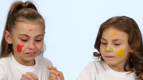 Children sit at the table and paint themselves on their faces with paint brushes Stock Footage 76128573