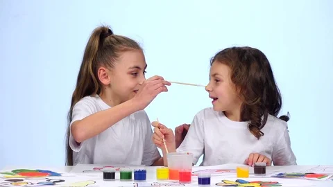 Children sit at the table and paint themselves on their faces with paint brushes Vidéo 76129391