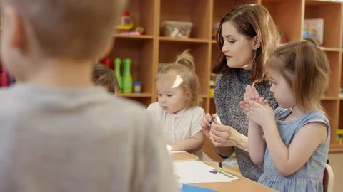 Children sit at the table and play with plasticine, kindergarten teacher shows Stock-Footage 108388740