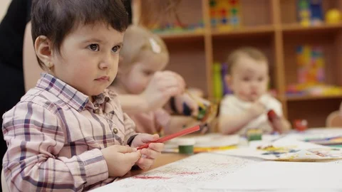 Children sit at the table, the child in the close view holding a red marker Stock Footage 108388980