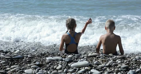 Children Sitting By The Beach And Throwing Stones In The Water Stock Footage 141924439