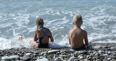 Children Sitting By The Beach And Throwing Stones In The Water Stock Footage 141924703
