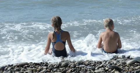 Children Sitting By The Beach And Throwing Stones In The Water Stock Footage 141924743