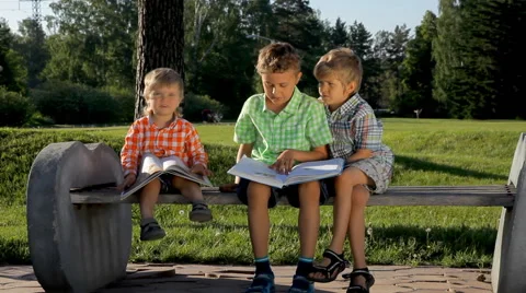 Children sitting on a bench and reading books in the park Stock Footage 52157785