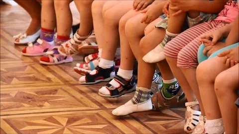 Children sitting in a row and moving their feet Stock Footage 77861370