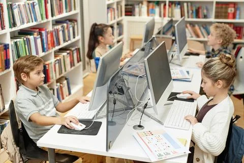 Children Sitting at Table with Computers in Lit Programming Class Stock Photos