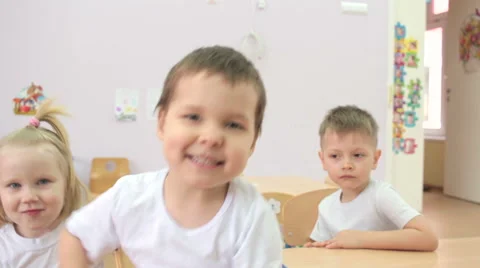 Children sitting at table waving  hands to camera. Vidéo 62196580