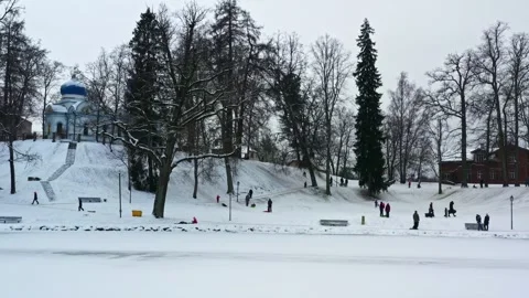 Children sledding down a snowy hill in a winter park with an orthodox church 스톡 동영상 335894260