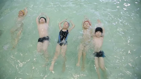 Children swim on their backs in the pool. Children in floating caps, learn to Video stock 117181948