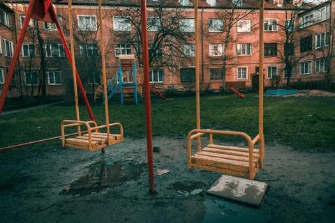 Children swing in empty courtyard of multi storey building, cloudy autumn day Stock Photos