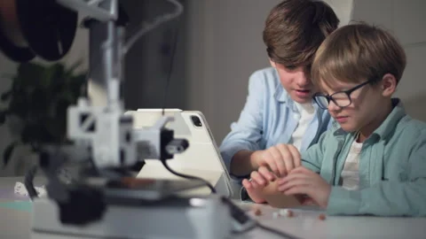 Children at a table with a working 3D printer, observing and operating it Stock Footage 335377598