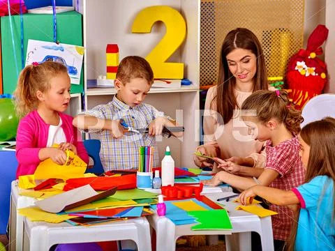 Children with teacher are making something out of colored paper. Stock Photos