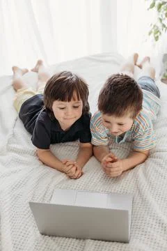 Children use technology. Online learning at home. The boys lie on the bed and Stock Photos