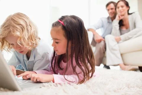 Children using a notebook while their parents are in the background Stock Photos